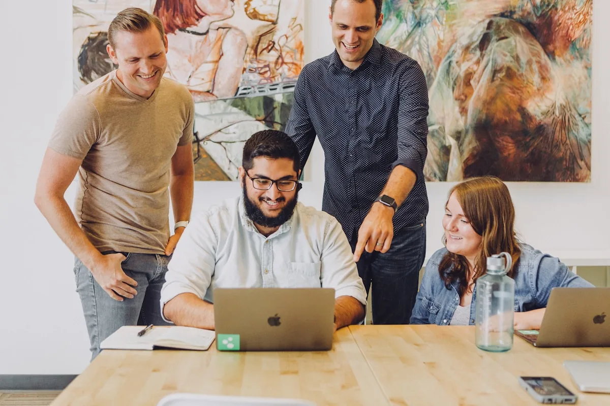 Four coworkers smiling and collaborating around a laptop